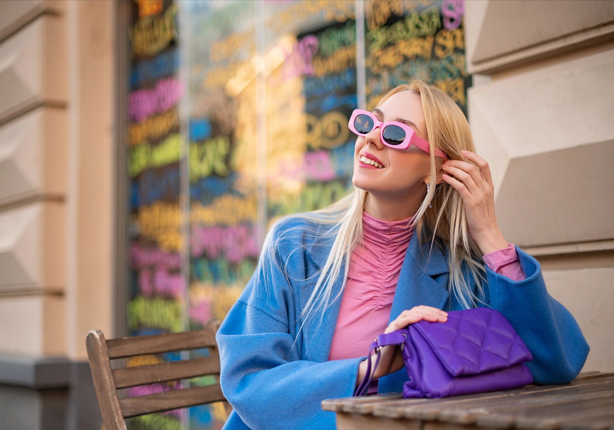 Fashionable woman wearing bright, colorful clothing, pink sunglasses, and a purple handbag | Be Bliss Boutique